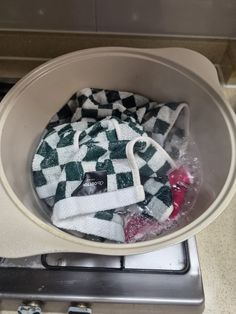 냄비의 뜨거운 물에 담긴 체크무늬 수건과 분홍색 걸레
